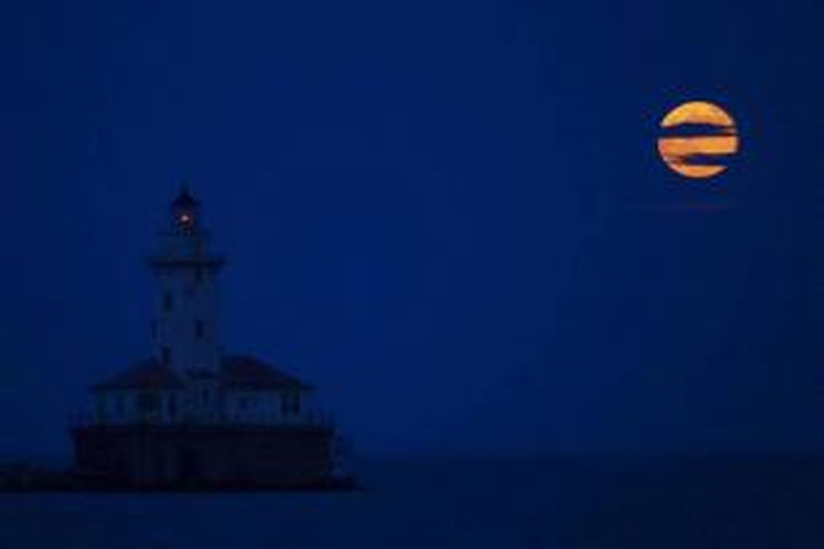 Bulan naik di sebelah Harbor Lighthouse Chicago, 23 Juni 2013, di Chicago. Bulan yang akan mencapai tahap penuh pada Minggu, 13.5 persen lebih dekat ke bumi dan dikenal sebagai fenomena supermoon.