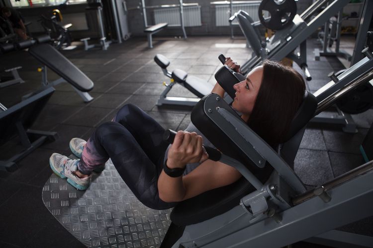 Ilustrasi seorang perempuan menggunakan alat hack squat di tempat gym.