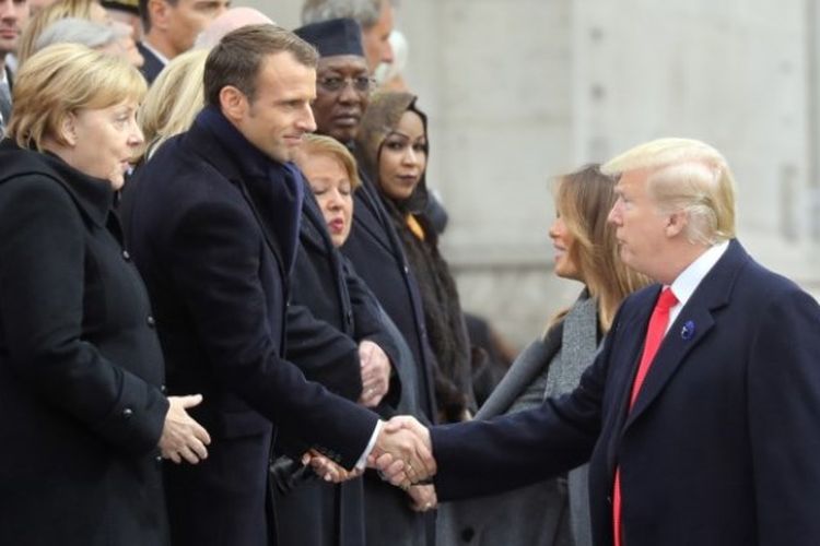 Presiden AS Donald Trump berjabat tangan dengan Presiden Prancis Emmanuel Macron dan Kanselir Jerman Angela Merkel, tiba bersama istrinya, Ibu Negara Pertama AS Melania Trump untuk menghadiri upacara di Arc de Triomphe di Paris, Minggu (11/11/2018). (AFP/Ludovic Marin)
