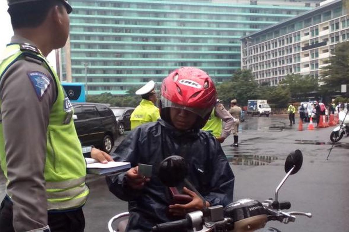 Salah seorang pengendara motor ditilang karena mencoba menerobos jalur pelarangan sepeda motor di Jalan M.H Thamrin, Jakarta Pusat, Senin (19/1/2015).