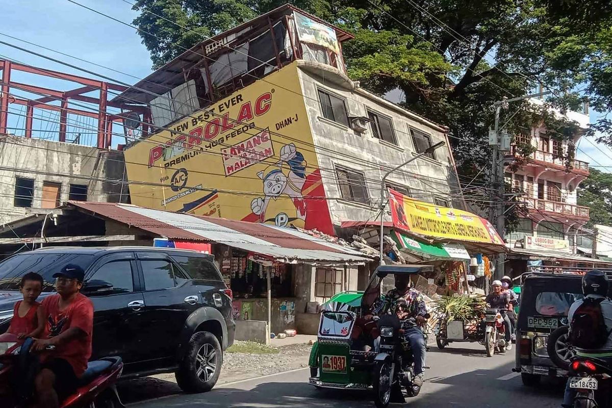 This handout photo taken and released by the Office of Abra Representative Ching Bernos shows people commuting past a damaged building in the municipality of Bangued, in the province of Abra on July 27, 2022, after a 7.0-magnitude earthquake hit the northern Philippines. (Photo by Handout / Office of Abra Representative Ching Bernos / AFP) 