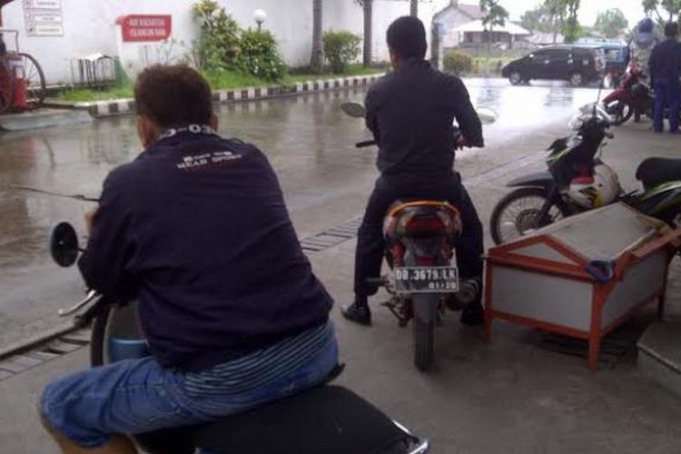 Pemotor berteduh di pom bensin saat hujan.