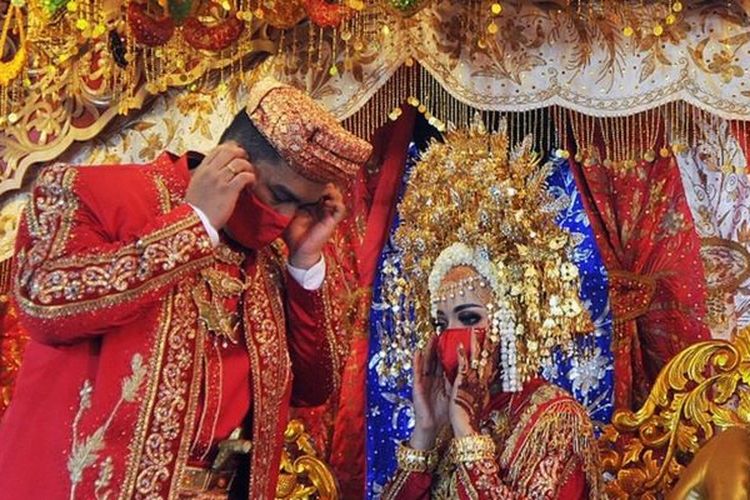 Pasangan pengantin merapikan masker saat resepsi pernikahan Minang atau Baralek, di Lubukbuaya, Padang, Sumatera Barat, 5 Juli lalu. Pemerintah daerah setempat sudah memperbolehkan warga menggelar pesta pernikahan saat masa normal baru seperti jaga jarak fisik, pengurangan kapasitas undangan, hidangan nasi kotak (bukan prasmanan) serta penerapan protokol kesehatan Covid-19.