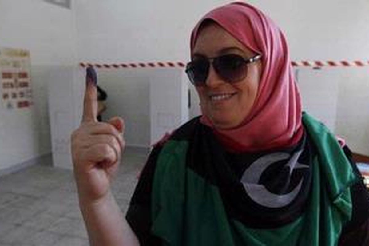 Membungkus pundaknya dengan bendera Libya, seorang perempuan memamerkan telunjuknya yang bertinta setelah memasukkan suara di sebuah tempat pemungutan suara di Benghazi, dalam pemilu legislatif pertama selama 40 tahun, Sabtu (7/7/2012). 