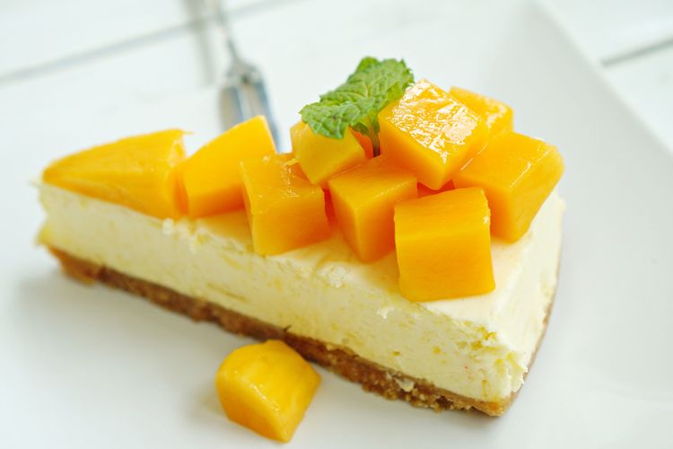 Ilustrasi cheesecake no bake rasa mangga dengan potongan mangga sebagai toppingnya.