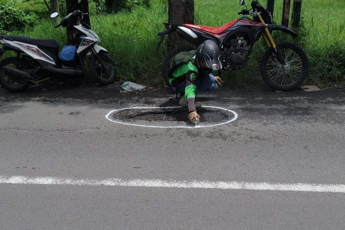 Driver gojek saat memberi tanda jalan berlubang di Jember agar pengendara terhindar dari kecelakaan