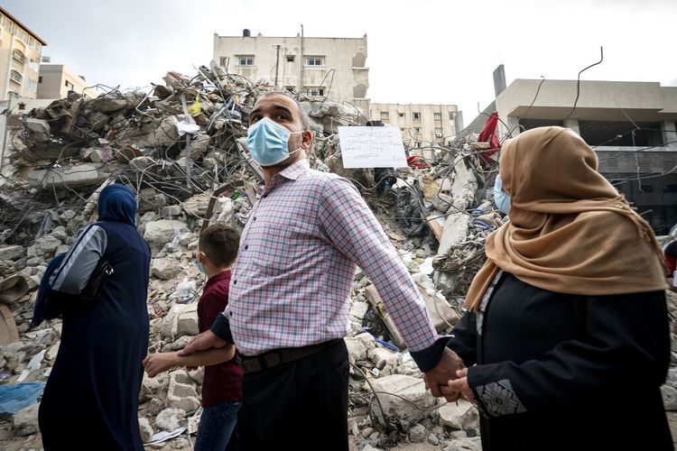 Sebuah keluarga melewati puing-puing dari sebuah bangunan yang sebelumnya hancur dalam serangan udara menyusul gencatan senjata yang dicapai setelah perang 11 hari antara penguasa Hamas Gaza dan Israel, di Kota Gaza, Jumat, 21 Mei 2021.