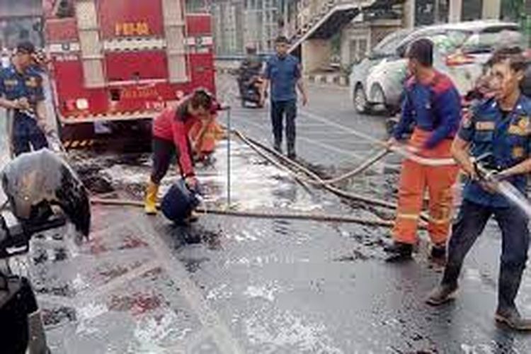 Petugas membersihkan tumpahan oli di jalan