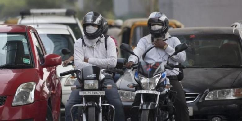 Pengendara motor menggunakan masker saat mengendarai kendaraannya melintasi jalanan kota New Delhi, India.