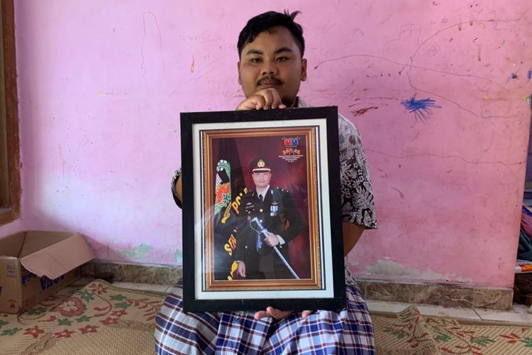 KEHILANGAN—Naufal Arozi (22) putra sulung almarhum Iptu Rochmat mengangkat foto ayahnya yang meninggal kemarin sore. Naufal merasa kehilangan sosok ayah kandungnya yang dikenal sebagai sosok bapak asuh bagi puluhan anak yatim-piatu di Jawa Timur.