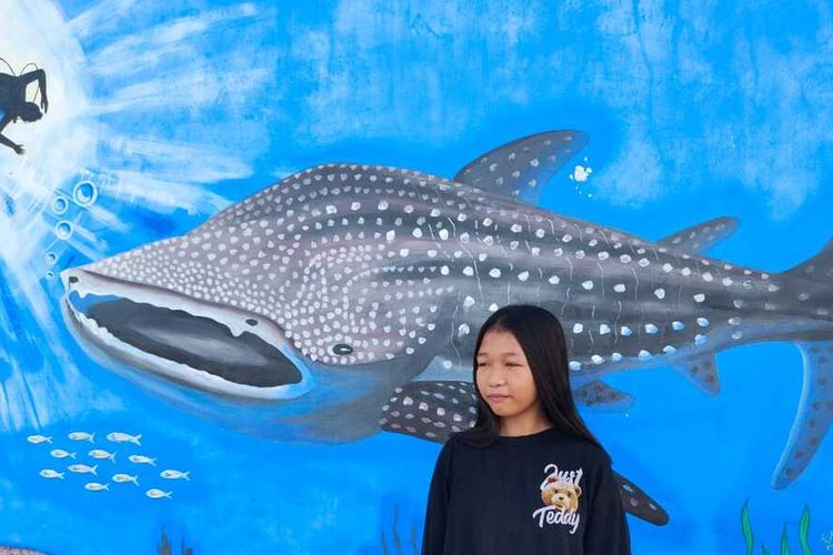 Sri Rahayu Ali di depan lukisan mural hiu paus di pantai Botubarani, Gorontalo, Rabu (3/4/2024). Gadis berumur 12 tahun kelas 6 SD ini memiliki pengalaman interaksi menarik dengan hiu paus. 