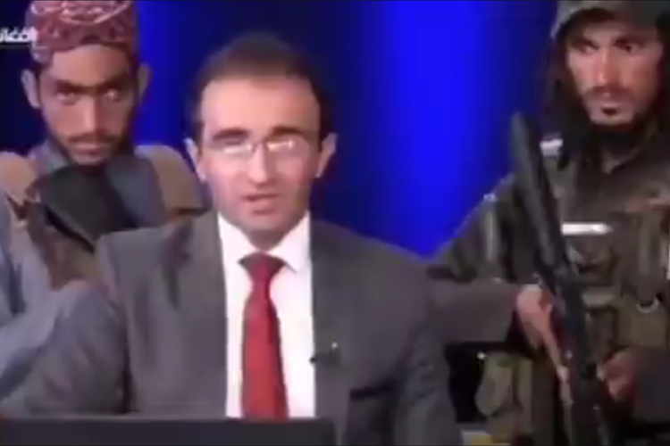 Tangkapan layara dari potongan video yang menunjukkan dua milisi Taliban berada di belakang pembawa acara program debat politik Pardaz dari saluran televisi Peace Studio Afghanistan.