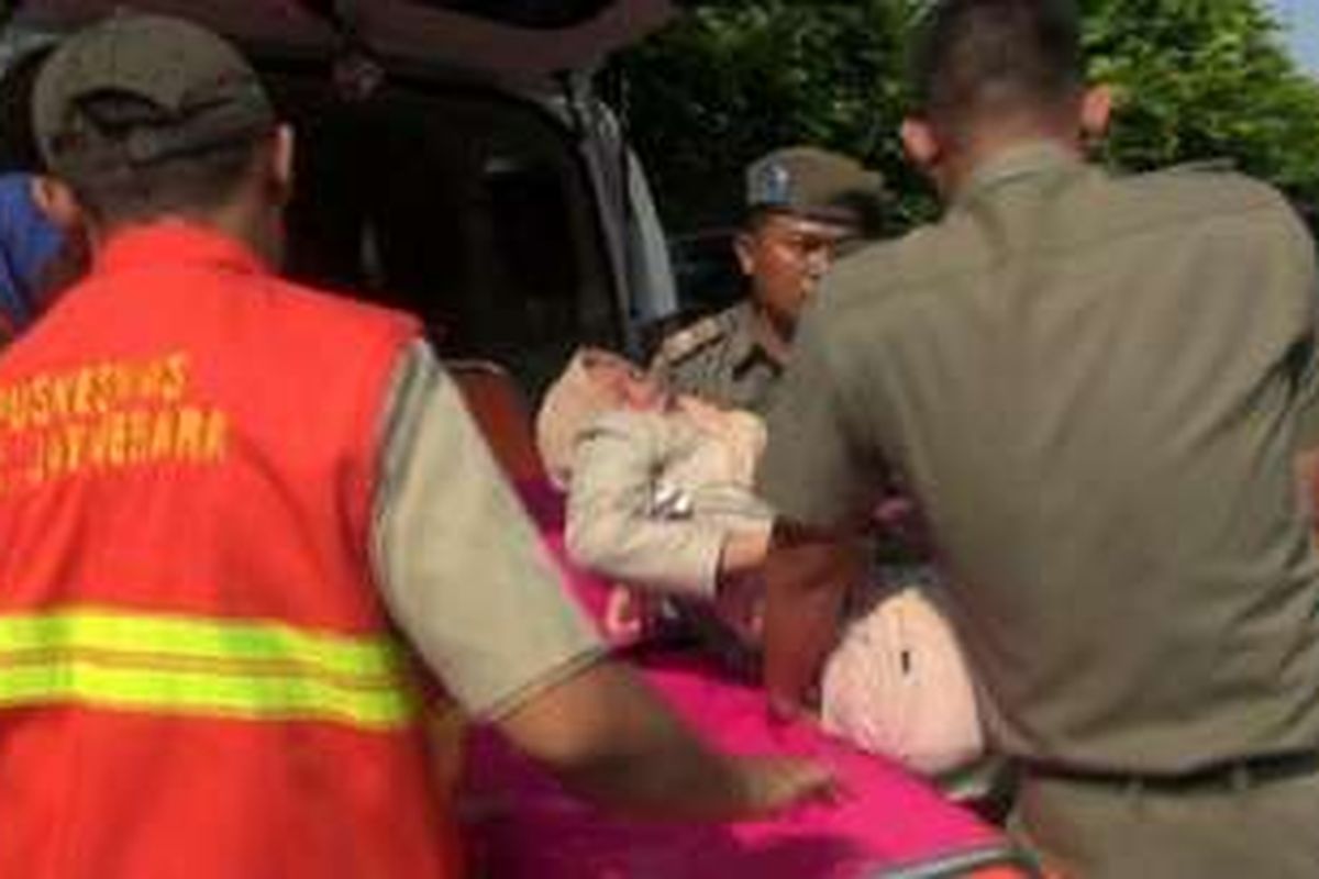 Petugas Puskesmas Kecamatan Jatinegara menggotong seorang Ibu yang pingsan saat antre daging murah bagi pemilik KJP di kantor Kecamatan Jatinegara, Jakarta Timur, Senin (27/6/2016). 