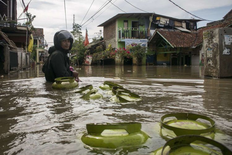 Warga membawa gas Elpiji 3 Kg saat melintasi banjir di Bojong Asih, Kabupaten Bandung, Jawa Barat, Jumat (8/3/2019). Sedikitnya 22 ribu kepala keluarga menjadi korban terdampak banjir di kawasan tersebut dengan 283 jiwa yang mengungsi akibat ketinggian air mencapai 40 cm sampai 280 cm.