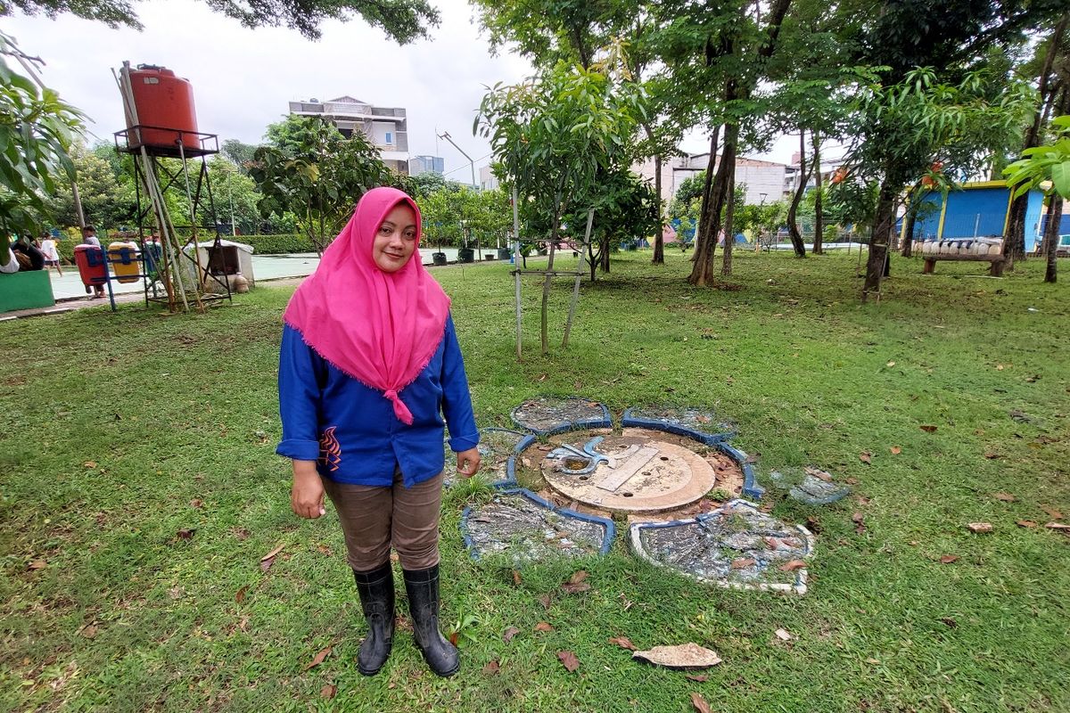 Pengelola RPTRA Kembangan, Opiani (36) berpose di depan sebuah sumur resapan yang didesain cantik berbentuk bunga, senada dengan taman bermain anak di sekitarnya, Selasa (8/11/2022).