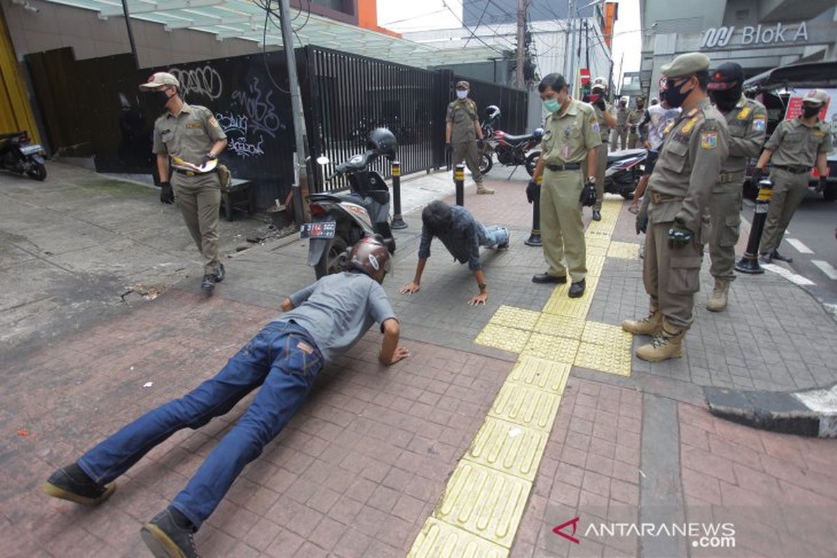 Petugas gabungan memberikan hukuman push up kepada warga yang tidak memakai masker saat razia penerapan aturan Pembatasan Sosial Berskala Besar (PSBB) di Kawasan Jalan Fatmawati, Jakarta, Selasa (28/4/2020).