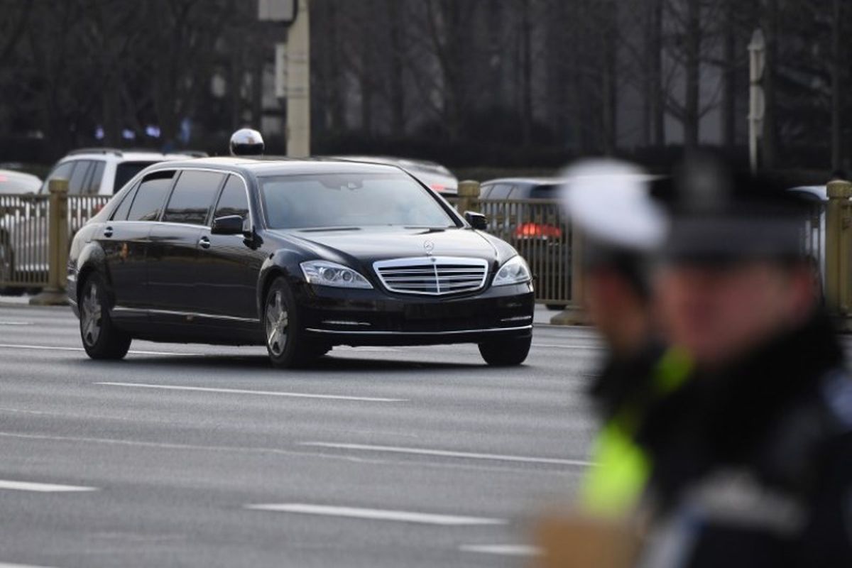 Mobil limosin dalam iring-iringan kendaraan pemimpin Korea Utara Kim Jong Un melewati polisi yang berjaga di sepanjang jalan utama timur-barat Changan di Beijing, China, Senin (9/1/2019). (AFP/Greg Baker)
