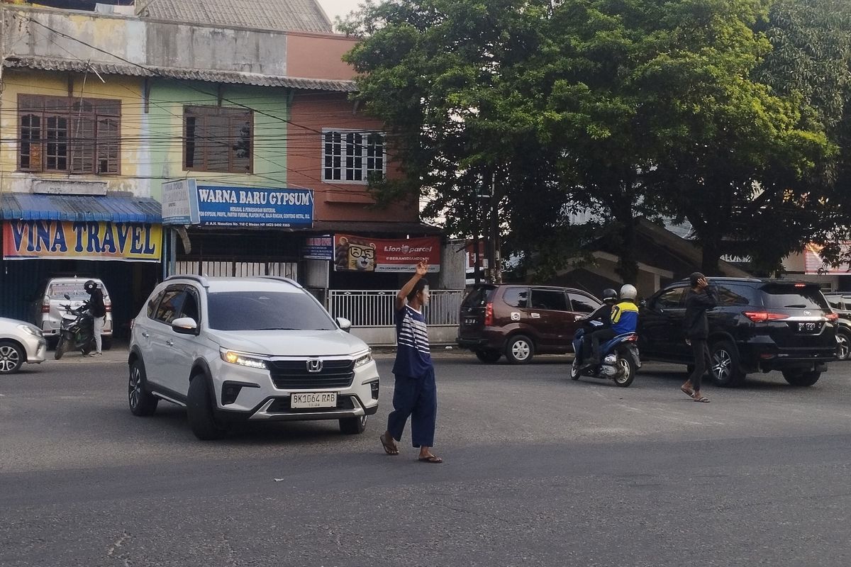 Pengatur lalu lintas informal atau pak ogah terlihat sedang membantu pengendara mobil untuk memutar arah di Jalan A.H Nasution, Kota Medan, Sabtu (16/8/2025)