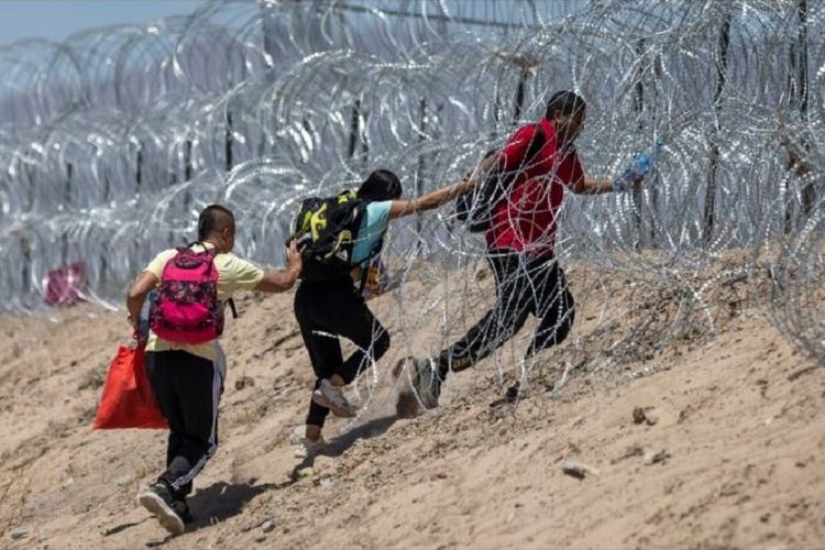 Imigran berjalan melewati pagar kawat berduri yang mengelilingi kamp migran darurat setelah melintasi perbatasan dari Meksiko pada 11 Mei 2023 di El Paso, Texas.