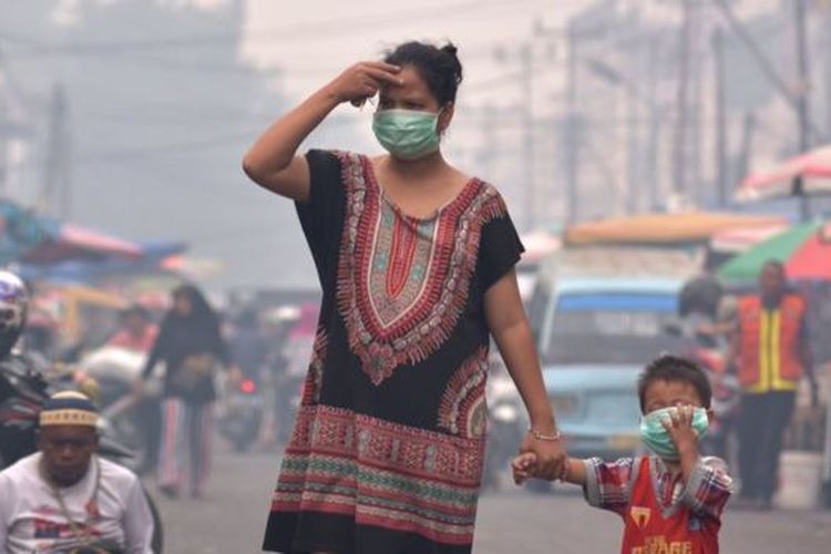 Seorang ibu dan anaknya mengenakan masker medis saat asap kebakaran hutan dan lahan (Karhutla) menyelimuti Kota Pekanbaru, Riau, Selasa (10/9/2019). 