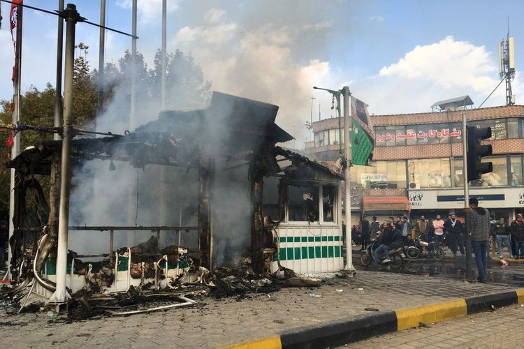 Warga iran berkumpul di sekitar pos polisi yang dibakar selama demonstrasi menentang kenaikan harga BBM di pusat kota Isfahan pada 17 November 2019.
