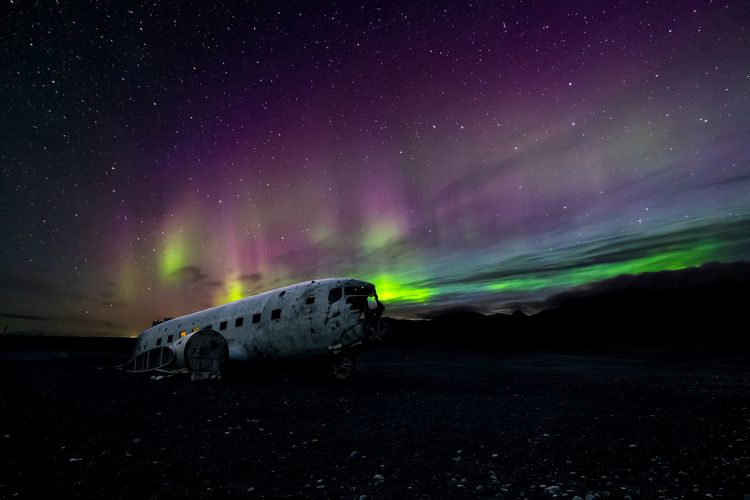 Bangkai pesawat di Islandia Selatan yang dihiasi Aurora Borealis di malam hari.