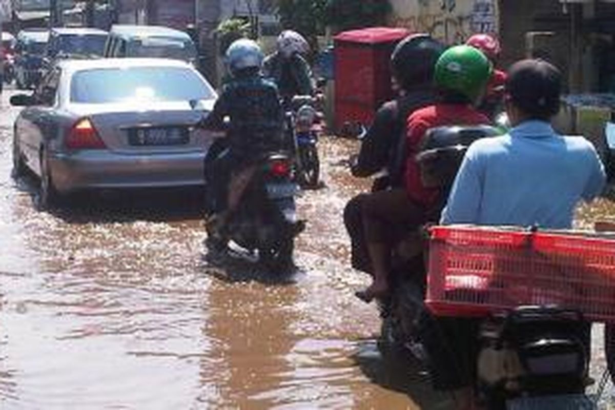 Jalan H Asmawi, Beji, Depok yang rusak menjadi kubangan lumpur. Hal itu membuat kendaraan melambatkan laju kendaraannya.