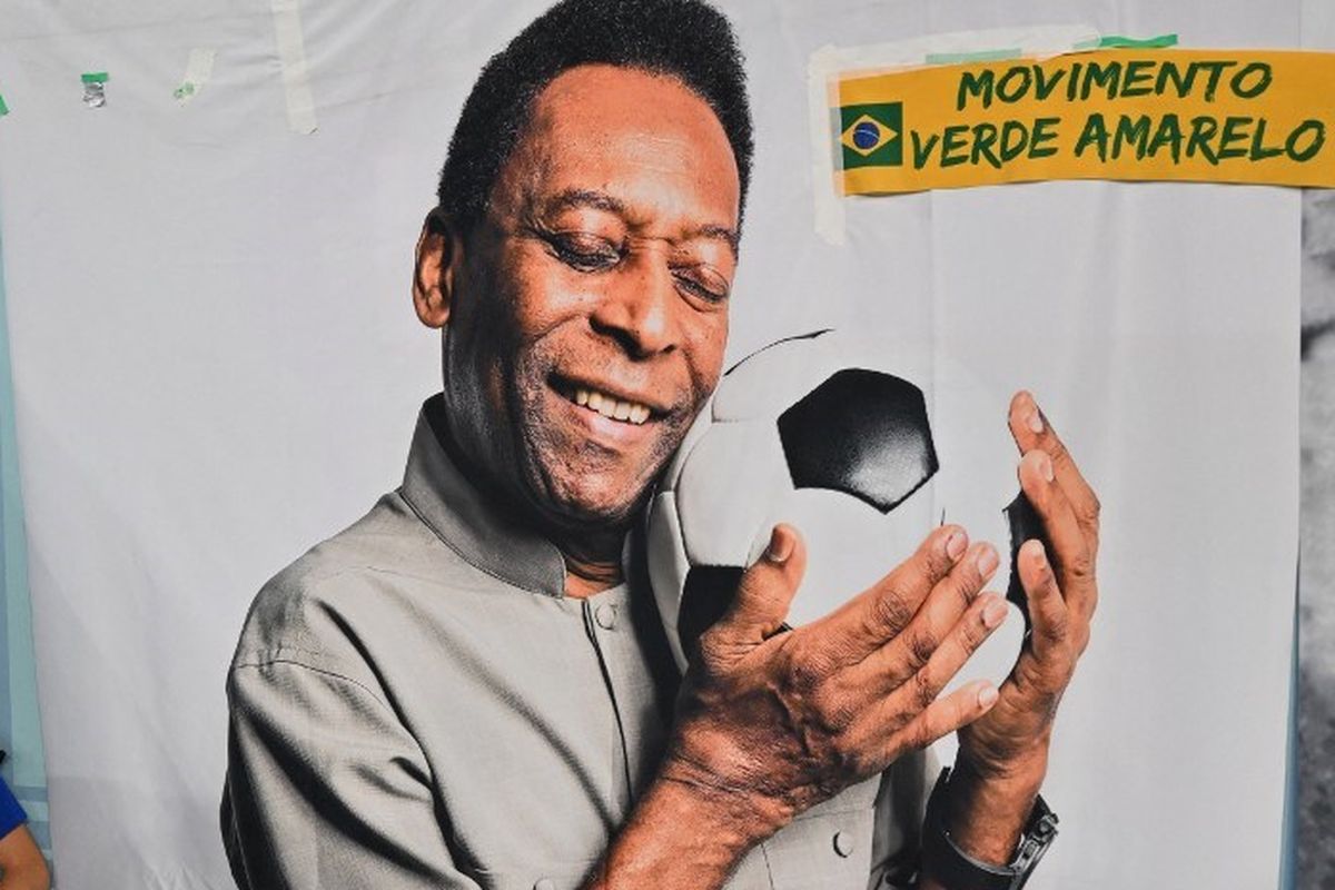 Seorang pekerja duduk di sebelah spanduk yang menggambarkan superstar sepak bola Brasil Pele selama pertandingan sepak bola putaran 16 besar Piala Dunia Qatar 2022 antara Brasil dan Korea Selatan di Stadion 974 di Doha pada 5 Desember 2022.