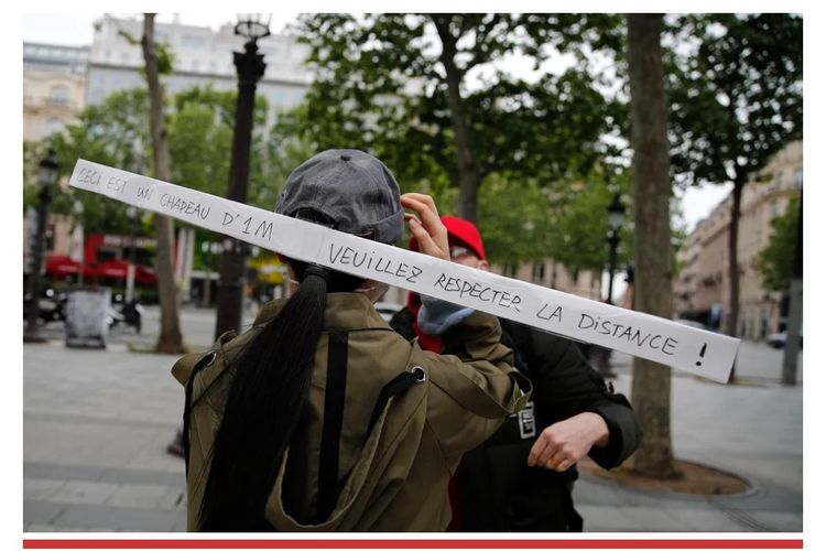 Seorang perempuan melintas di sebuah jalan di Paris dengan topi bertanda khusus. Tanda tersebut memiliki tulisan untuk meminta orang menjaga jarak demi mencegah penularan Covid-19.0