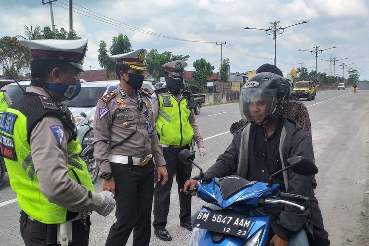 Petugas gabungan memberhentikan pengendara sepeda motor yang tidak menggunakan masker saat menuju Kota Pekanbaru yang telah menetapkan PSBB mulai hari ini, Jumat (17/4/2020).