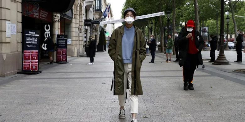 Seorang perempuan melintas di sebuah jalan di Paris dengan topi bertanda khusus. Tanda tersebut memiliki tulisan untuk meminta orang menjaga jarak demi mencegah penularan Covid-19.0