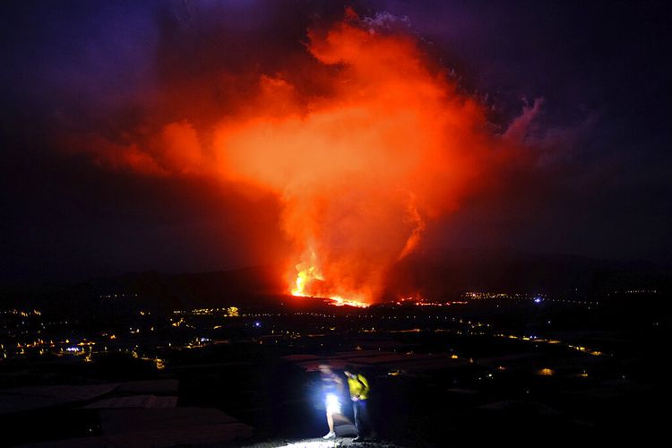 Dua orang berjalan saat lava menyembur dari gunung berapi di pulau Canary La Palma, Spanyol pada dini hari Sabtu 25 September 2021. 