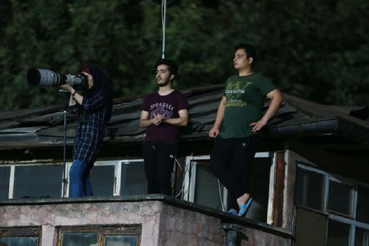 Dalam foto terlihat Parisa Pourtaherian (paling kiri) memotret jalannya pertandingan sepak bola antara Nassaji Mazandaran melawan Zob Ahan dari atap rumah di kota Ghaemshahr. Pourtaherian terpaksa memanjat atap karena perempuan dilarang masuk stadion sepak bola.