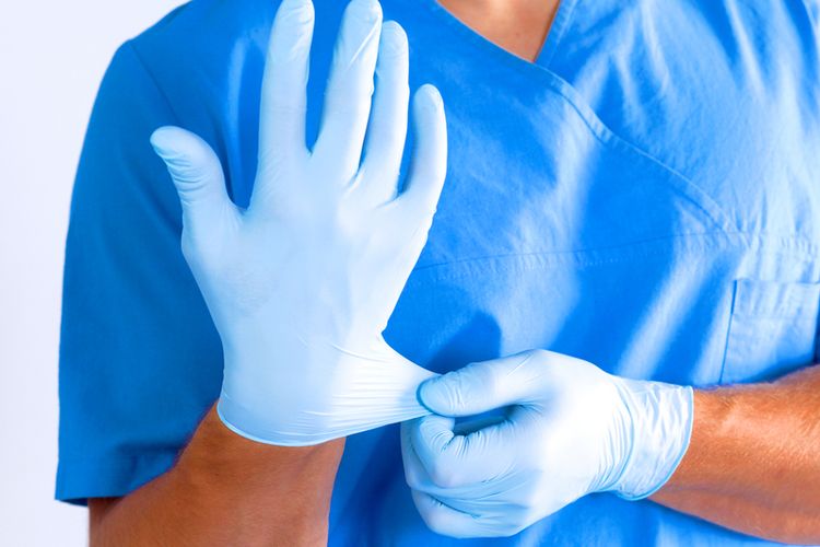 Seorang tenaga medis memakai sarung tangan lateks