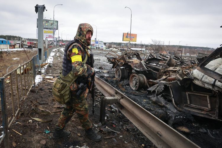 Seorang pria bersenjata berdiri di dekat sisa-sisa kendaraan militer Rusia di Bucha, dekat ibu kota Kyiv, Ukraina, Selasa, 1 Maret 2022. 