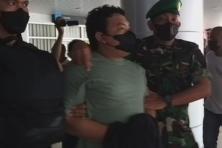 Seorang oknum TNI Kodam XVI Pattimura, Kopda TH dengan kedua tangan tertutup digelandang petugas Denpom Pattimura saat tiba di Bandara Pattimura Ambon Minggu (16/1/2022).