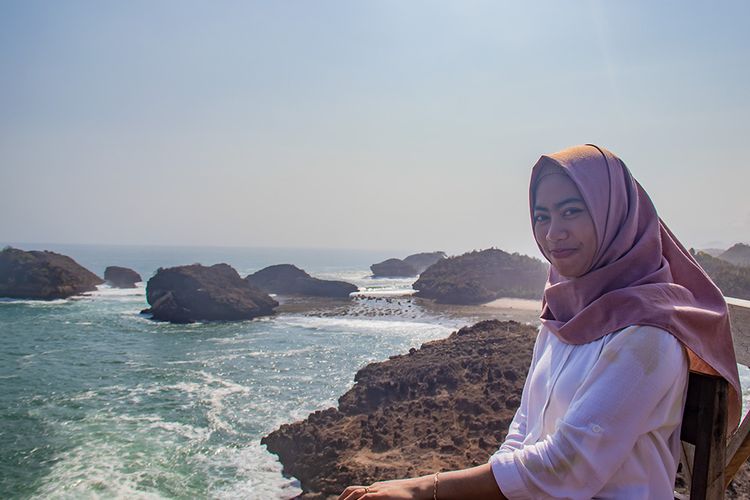 Seorang pengunjung berfoto dengan latar belakang gugusan karang di Pantai Kasap, Pacitan.