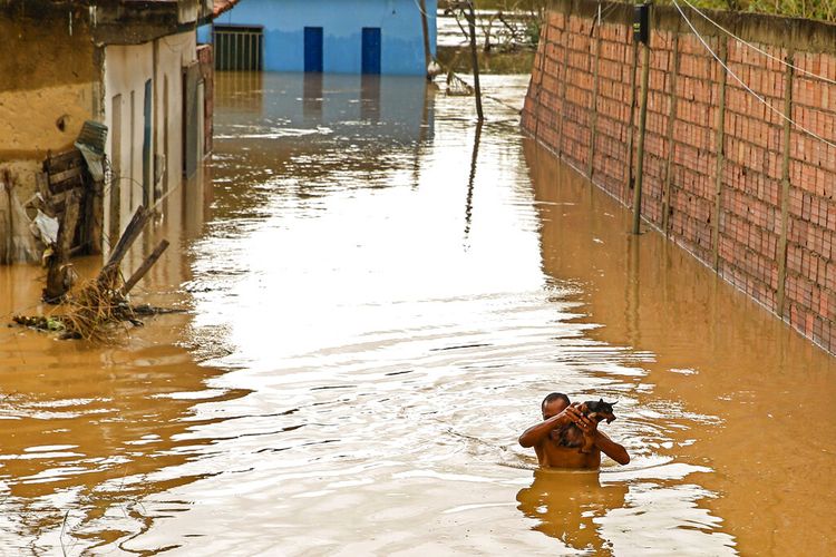 Seorang pria membawa anjingnya melewati banjir di Itapetinga, negara bagian Bahia, Brasil, Senin, 27 Desember 2021. 