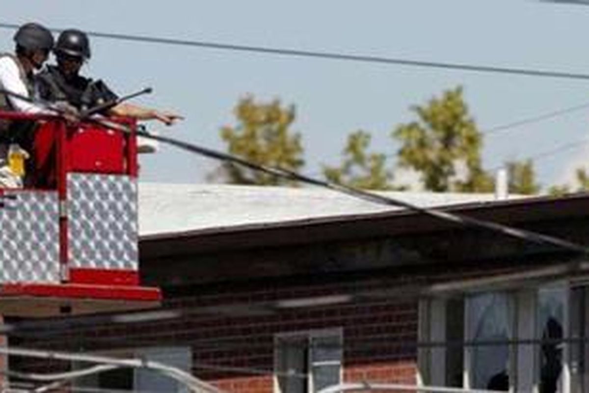 Polisi menggunakan peralatan milik pemadam kebakaran berusaha melihat ke dalam apartemen James Holmes.