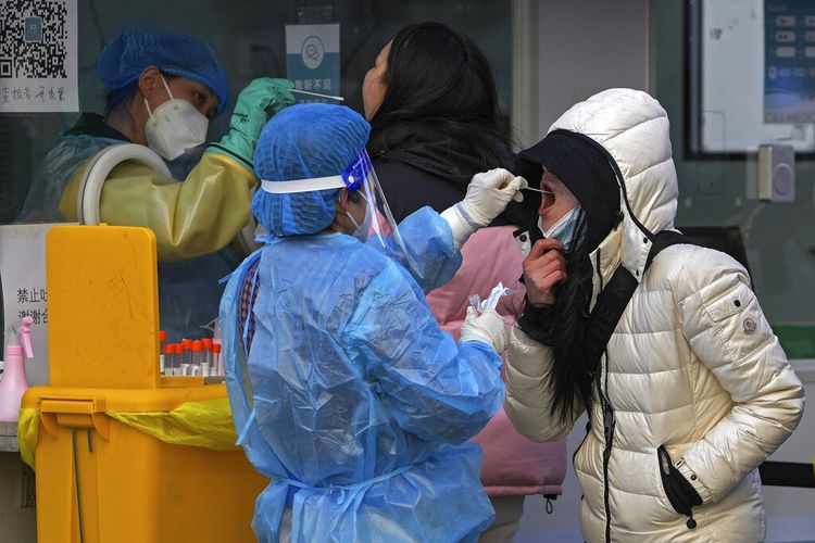 Orang-orang mendapatkan swab untuk tes COVID-19 untuk persyaratan bepergian di fasilitas pengujian virus corona seluler di luar gedung perkantoran komersial di Beijing, Minggu, 26 Desember 2021.