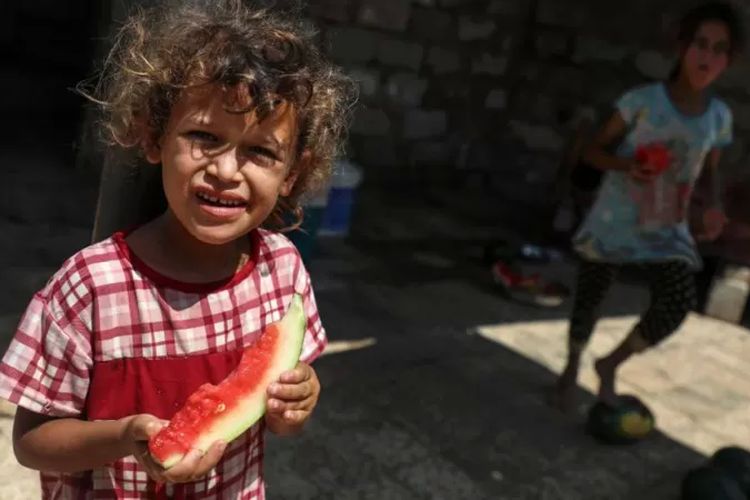 Anak-anak Palestina sedang menikmati semangka di pinggiran Kamp Pengungsi Khan Younis, di selatan Jalur Gaza, pada 22 Juli 2020.