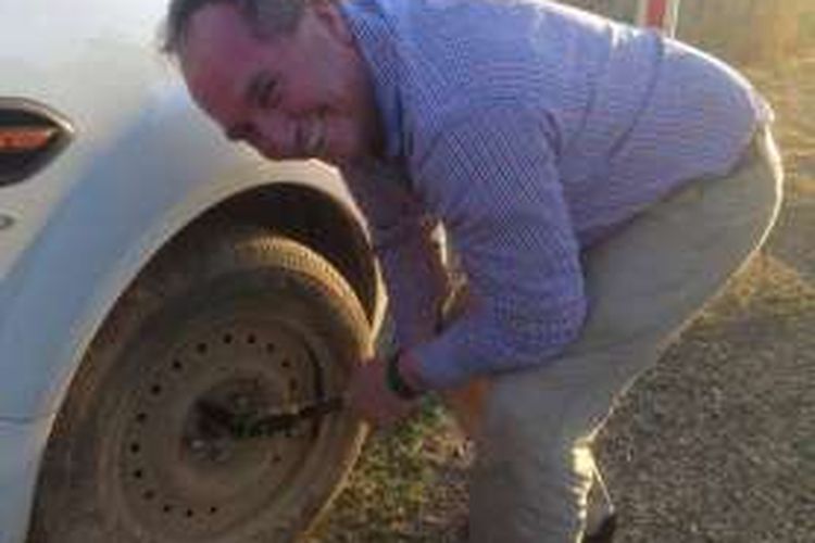 Wakil PM Barnaby Jones sedang mengganti ban mobil milik seorang pengemudi perempuan.