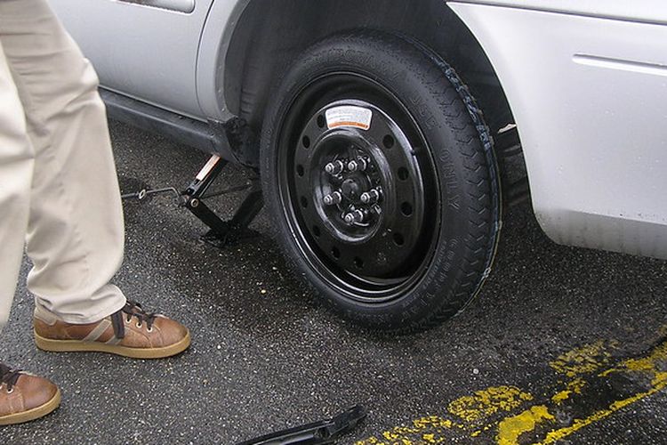 Ilustrasi pengemudi mengganti ban bocor dengan ban cadangan jenis temporary tire