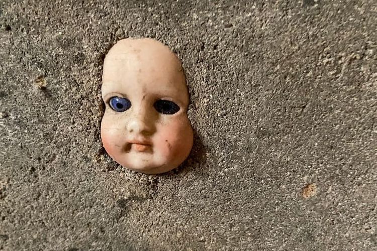 Kepala boneka bayi yang tertanam di tembok ruang bawah tanah rumah.  