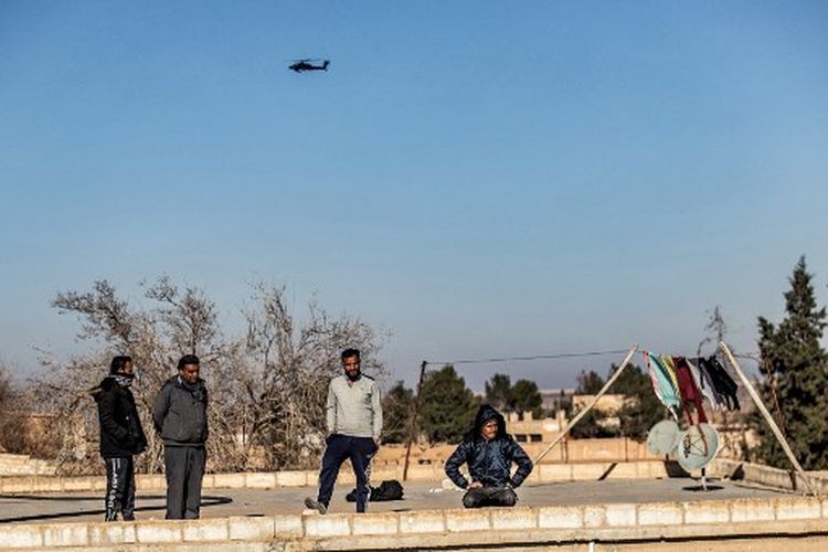 Penduduk setempat menyaksikan helikopter serang A AS AH-64 Apache terbang di atas tentara AS yang berpatroli di sepanjang garis depan antara daerah yang dikuasai oleh Pasukan Demokratik Suriah (SDF) dan pejuang yang didukung Turki di dekat desa Dardara di pedesaan Tal Tamr di timur laut Suriah Provinsi Hasakeh pada 26 Desember 2021. 