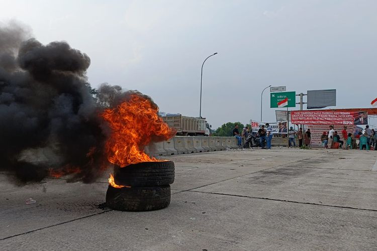 Demo lanjutan para warga atas ganti rugi hak tanah di Tol Jatikarya pada Selasa (12/7/2022) siang. Selain membakar dua buah ban mobil bekas sekaligus, warga juga membentangkan sebuah spanduk protes kepada Menteri ATR/BPN yakni Hadi Tjahjanto. 