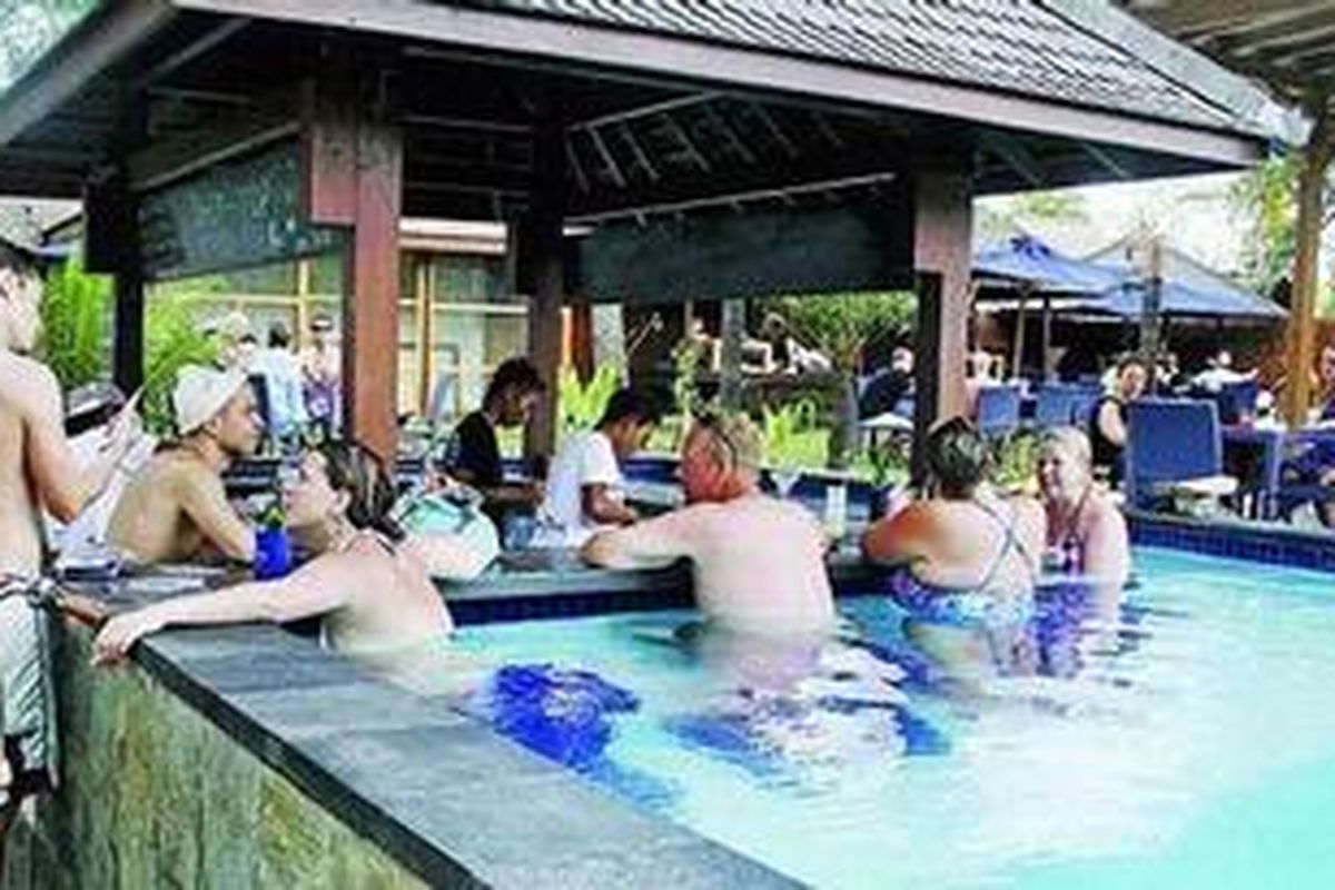 Serombongan wisatawan menikmati suasana siang dengan berendam di kolam renang sambil menikmati minuman dan sajian menu lain di Gili Trawangan. Tempat itu banyak dikunjungi turis muda usia. 