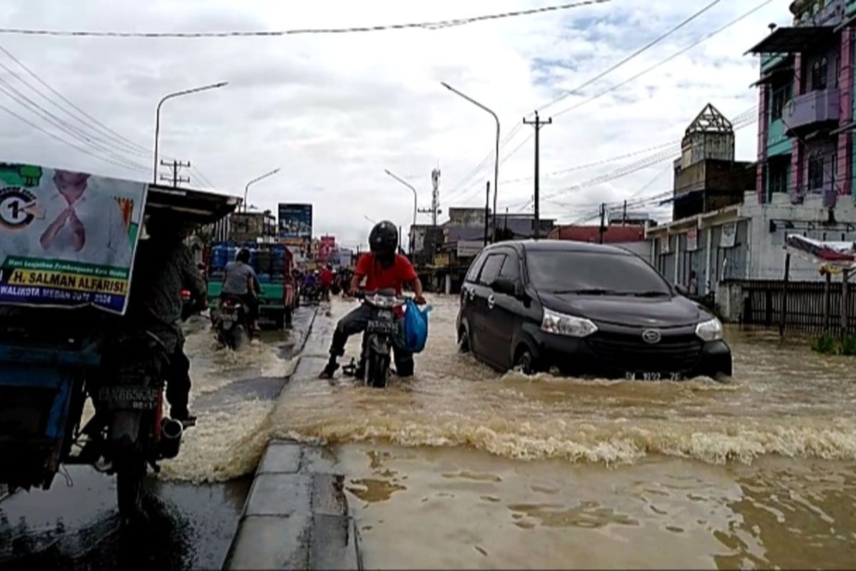 Seorang warga mendorong sepeda motor yang mogok saat melintasi banjir di Desa Lalang, Kecamatan Sunggal, Deli Serdang pada Jumat (4/12/2020).