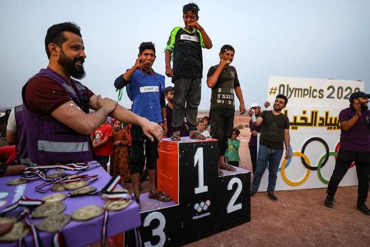 Anak laki-laki Suriah yang terlantar berdiri di podium setelah memenangkan medali selama Olimpiade Perkemahan 2020 di kota Fuaa, di benteng pemberontak besar terakhir Suriah di barat laut Idlib, pada Sabtu (7/8/2021). [OMAR HAJ KADOUR/AFP]