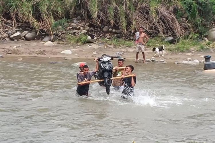 Foto : Warga memikul motor di kali Korobhera menuju Desa Korobhera Kecamatan Mego, Kabupaten Sikka, NTT, Senin (3/1/2021).